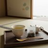 和室の畳の上で、湯呑みに注がれた黄金色の阿波晩茶とティーバッグ、急須が木製トレーに載っている様子。